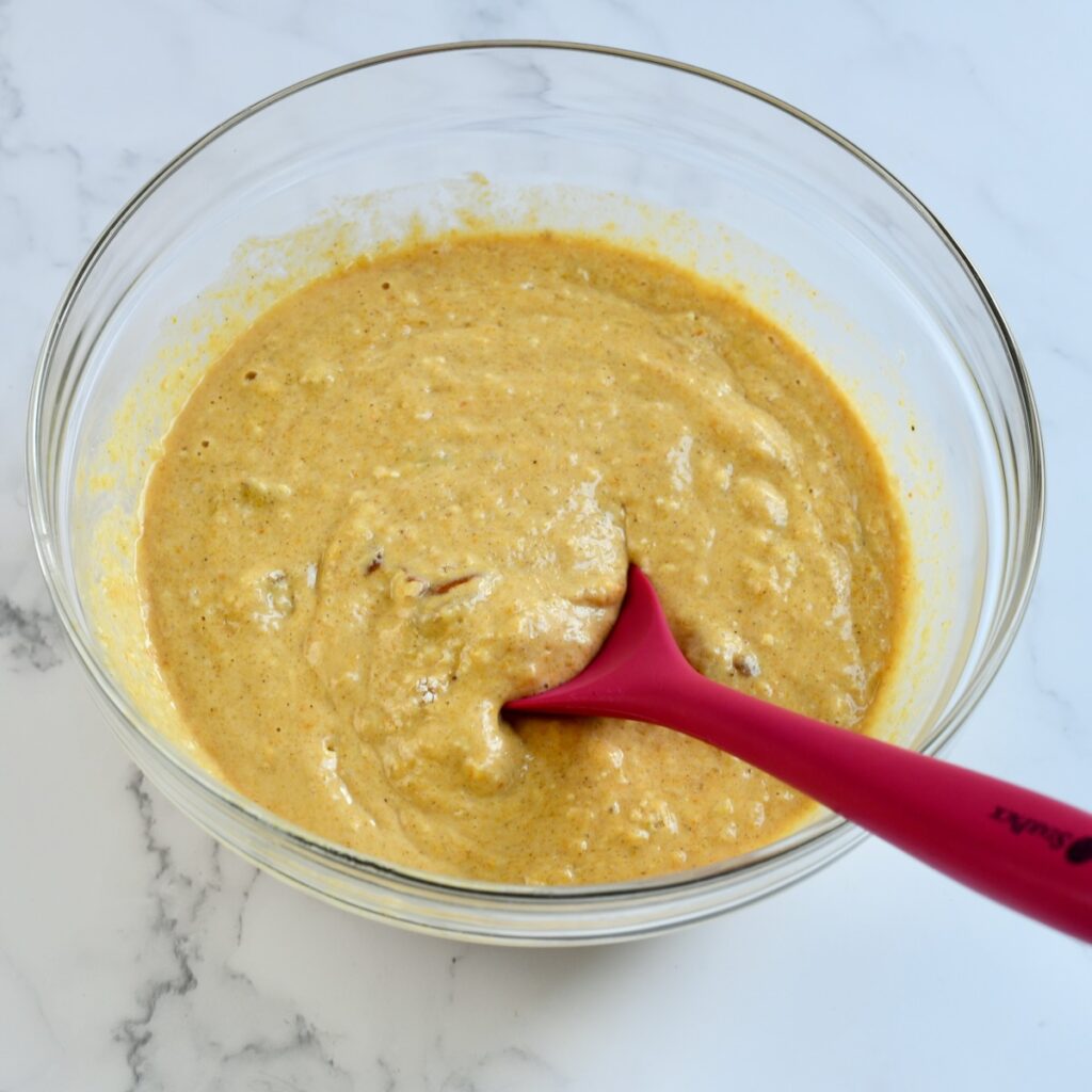 Red spoonula in pumpkin pecan waffle batter in clear bowl.