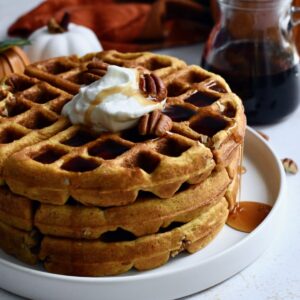 Pecan Pumpkin Belgian Waffles stacked with maple syrup and whipped cream.
