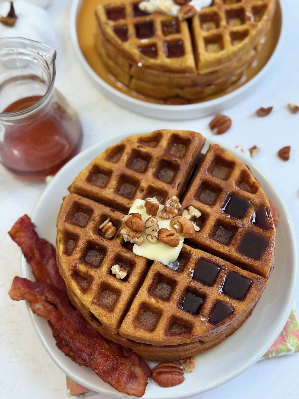 Pecan pumpkin waffles with bacon on a white plate.