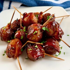 Close up of bacon wrapped meatballs piled onto a plate.