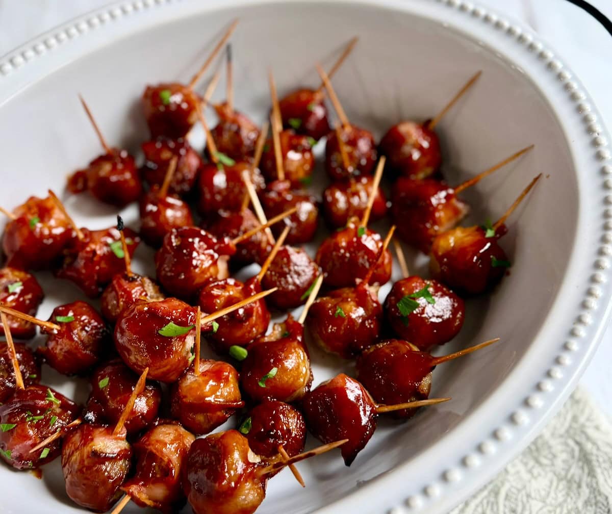 Bacon wrapped meatballs served in a serving dish with toothpicks.