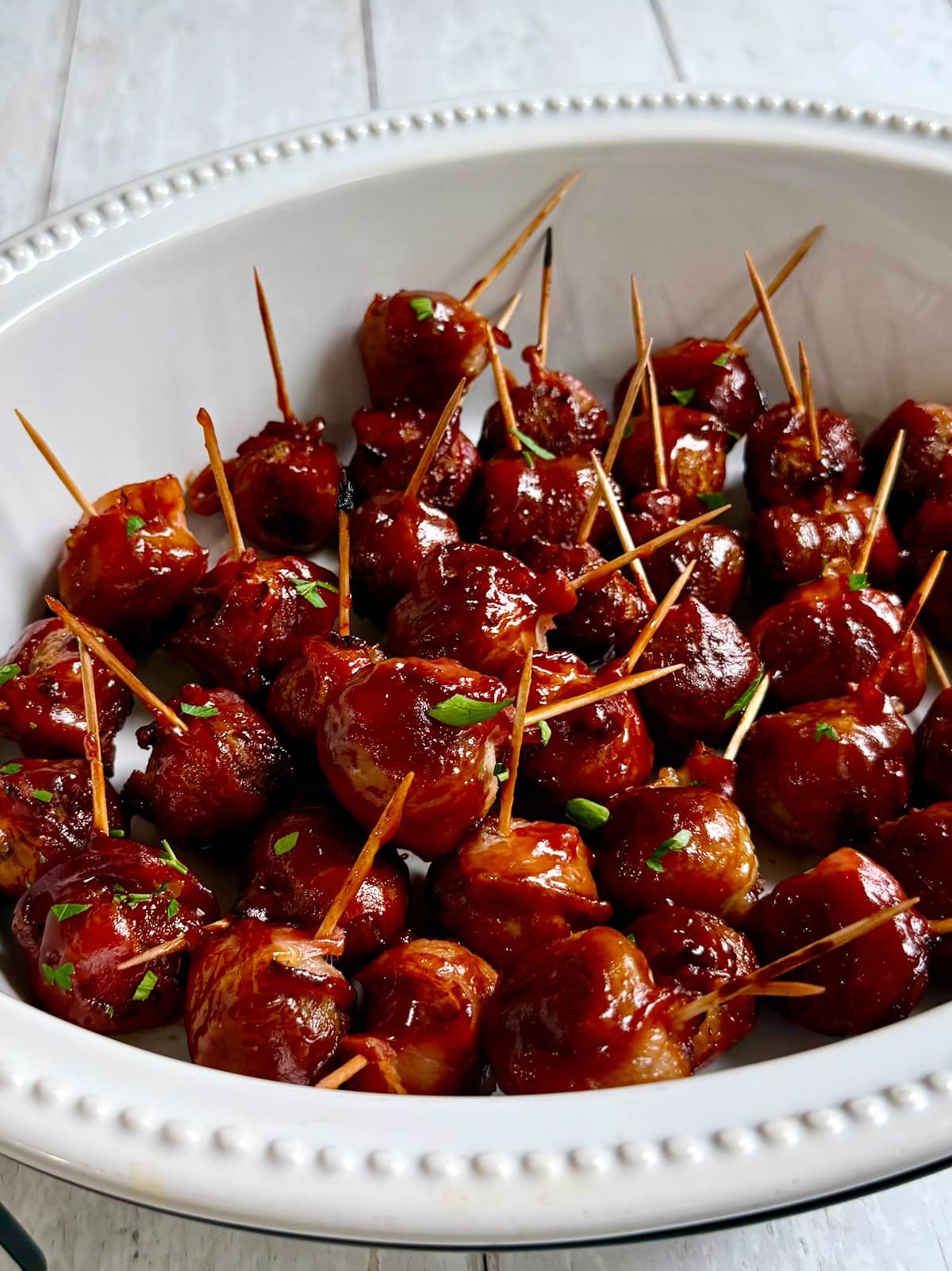 Bacon wrapped meatballs with toothpicks in them served in a white serving dish.