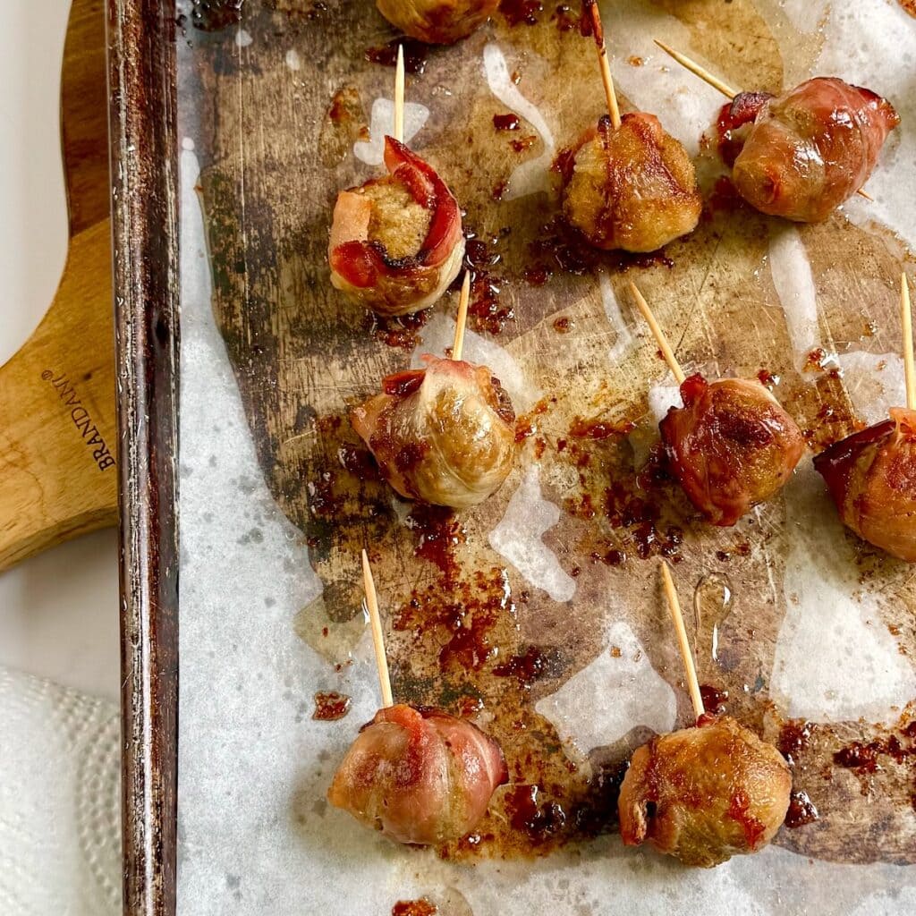 Baked bacon wrapped meatballs on a sheet pan.