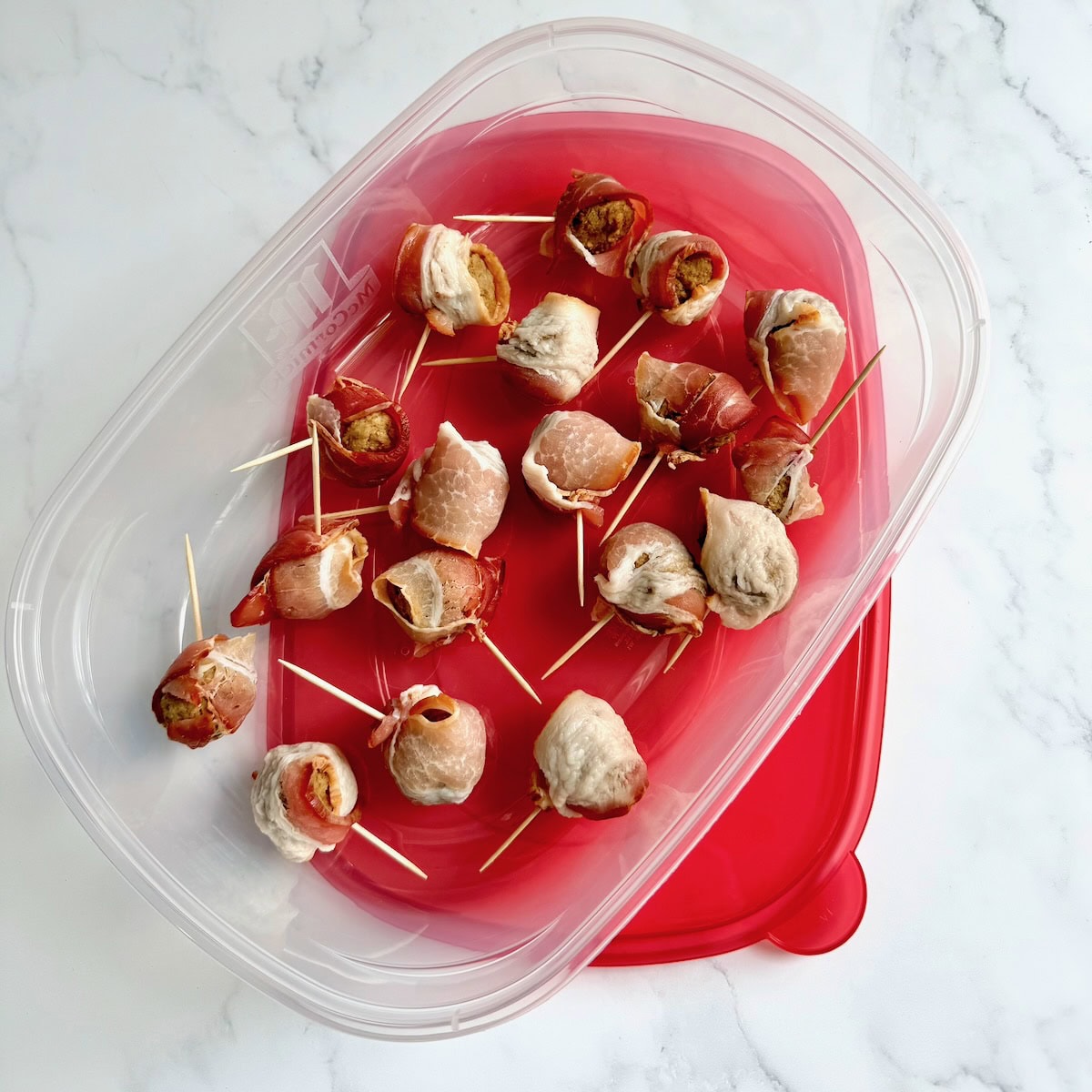 Bacon wrapped meatballs prepped and placed in a plastic container.