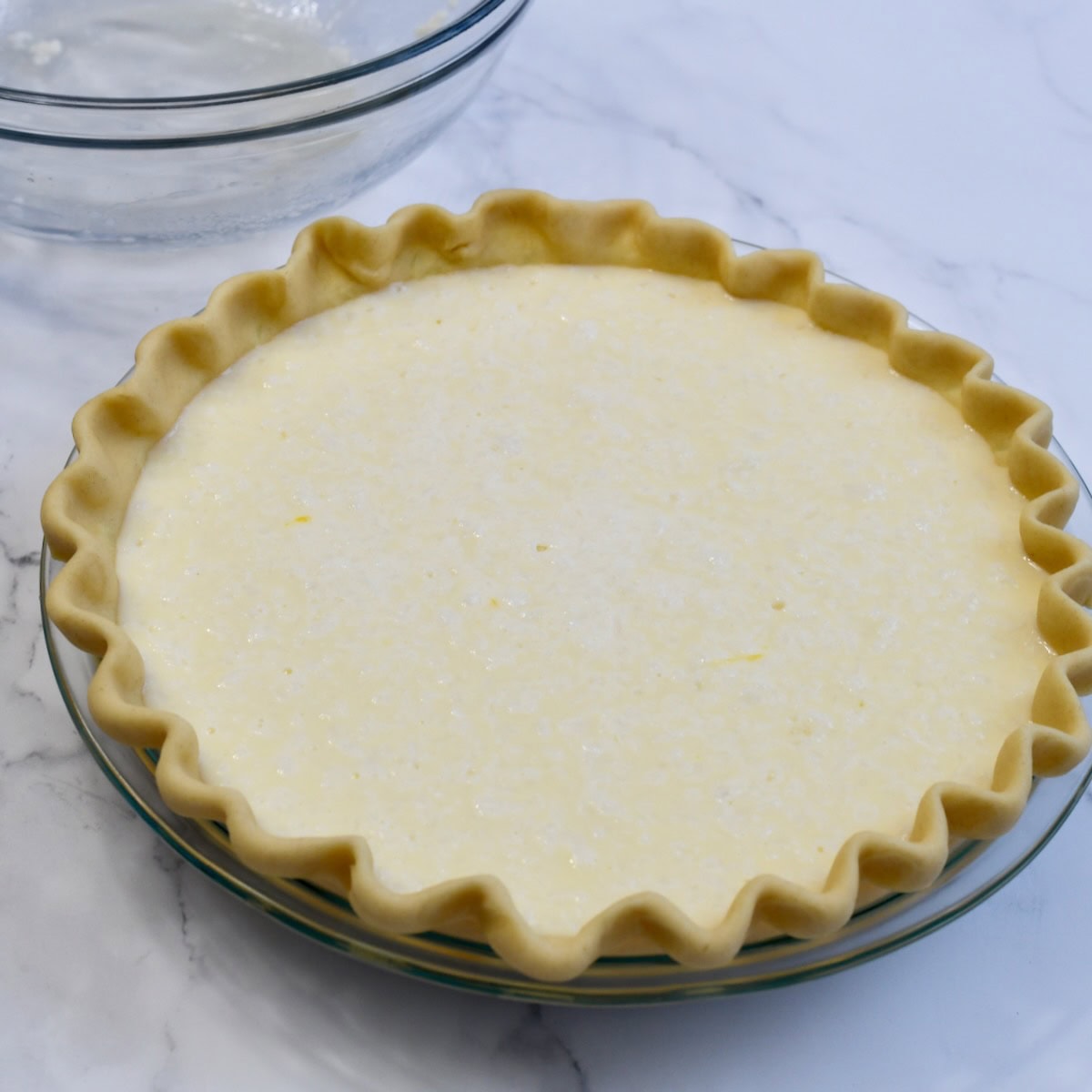 Unbaked pie shell in a glass pie plate is filled with coconut custard filling before baking.
