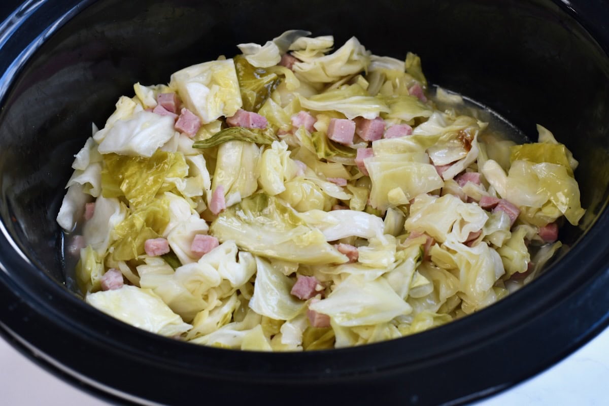 Crock pot ham and cabbage in a black slow cooker.