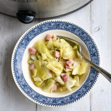 A blue and white bowl with crock pot ham and cabbage and a fork resting on the side.