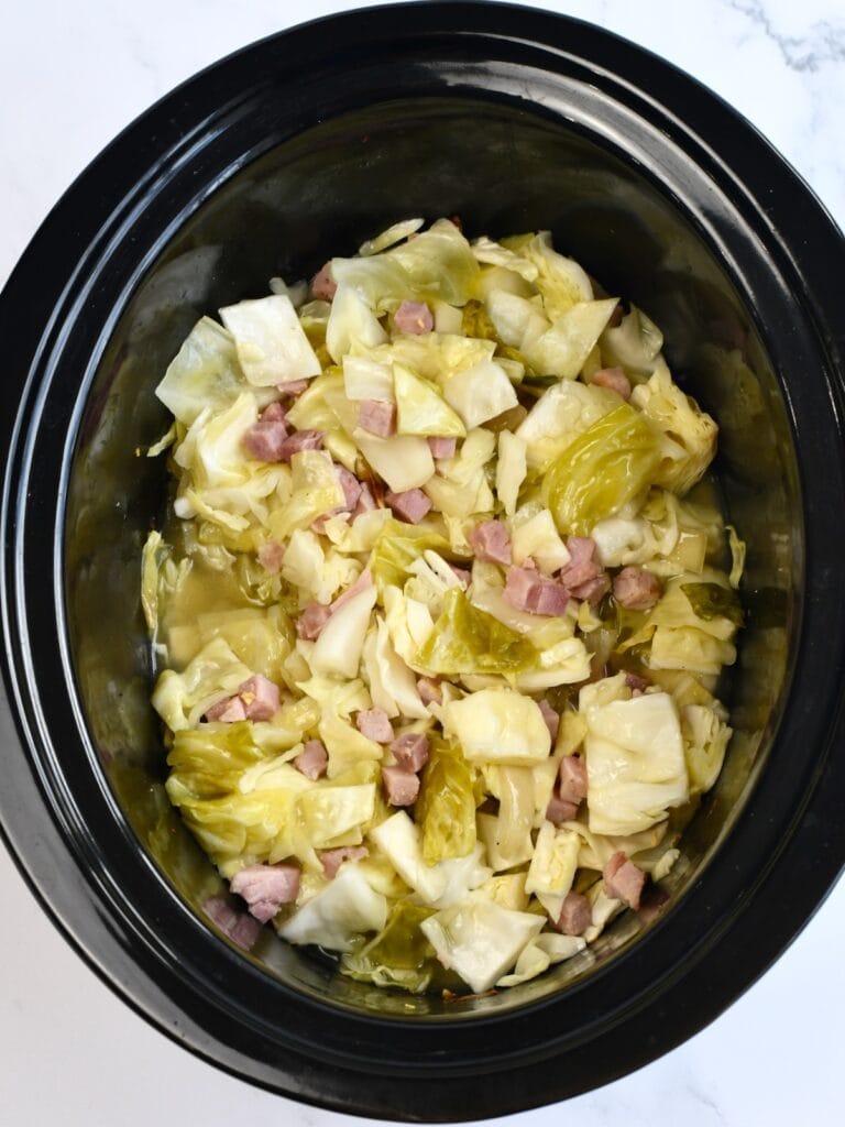 A black slow cooker bowl with cabbage and ham.