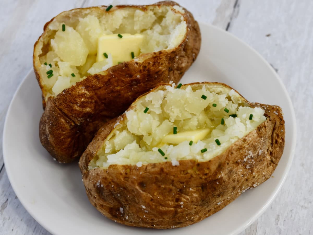 Two russet potatoes served on a plate with butter and chives on top.