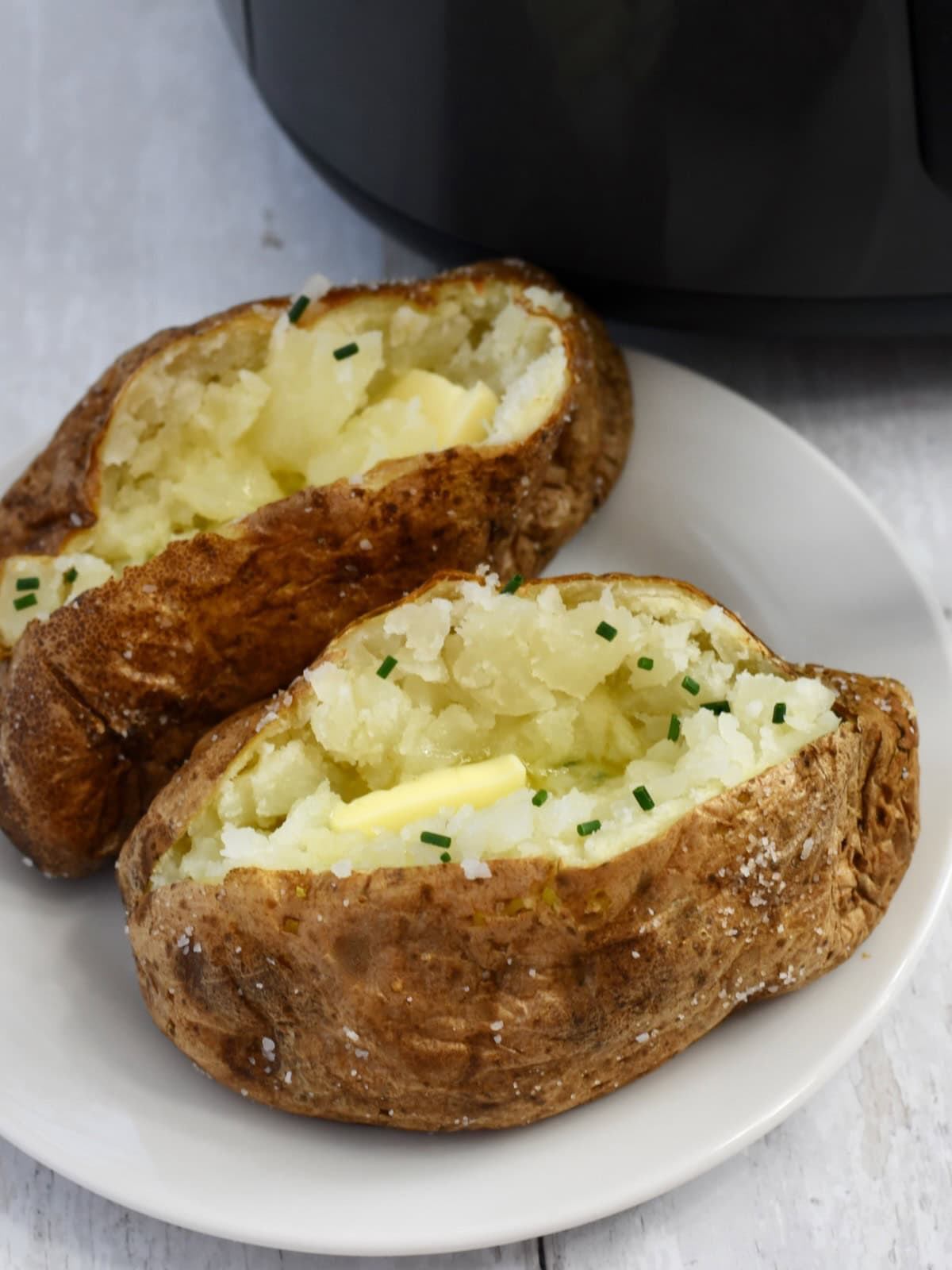 Two baked potatoes on a plate, sliced open and garnished with butter and chives.