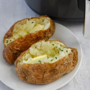 Two baked potatoes served on a plate both garnished with butter and chives.