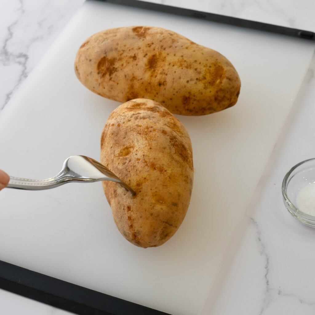 Fork poking the russet potatoes with holes on a cutting board.