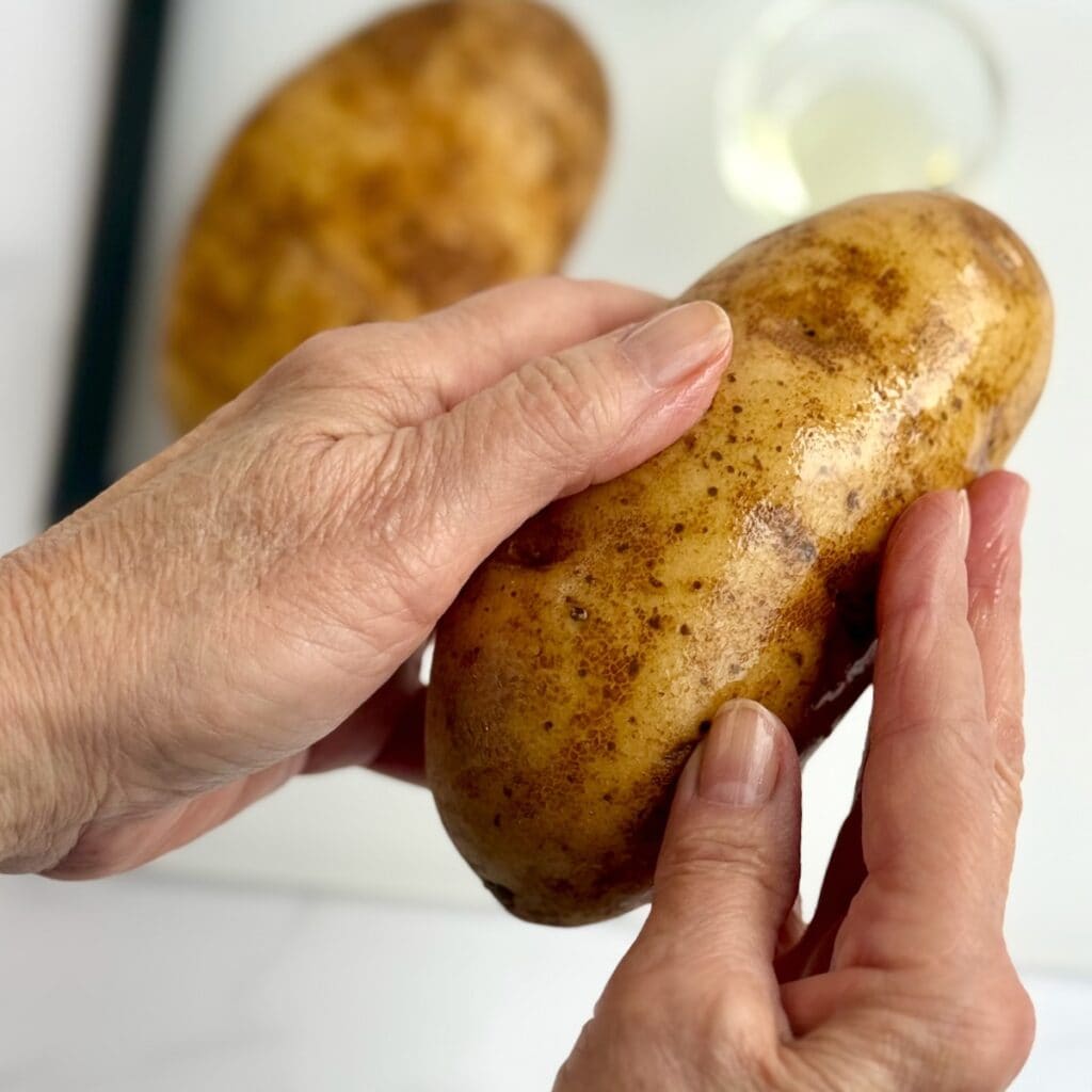 Hands rubbing a russet potato with cooking oil.