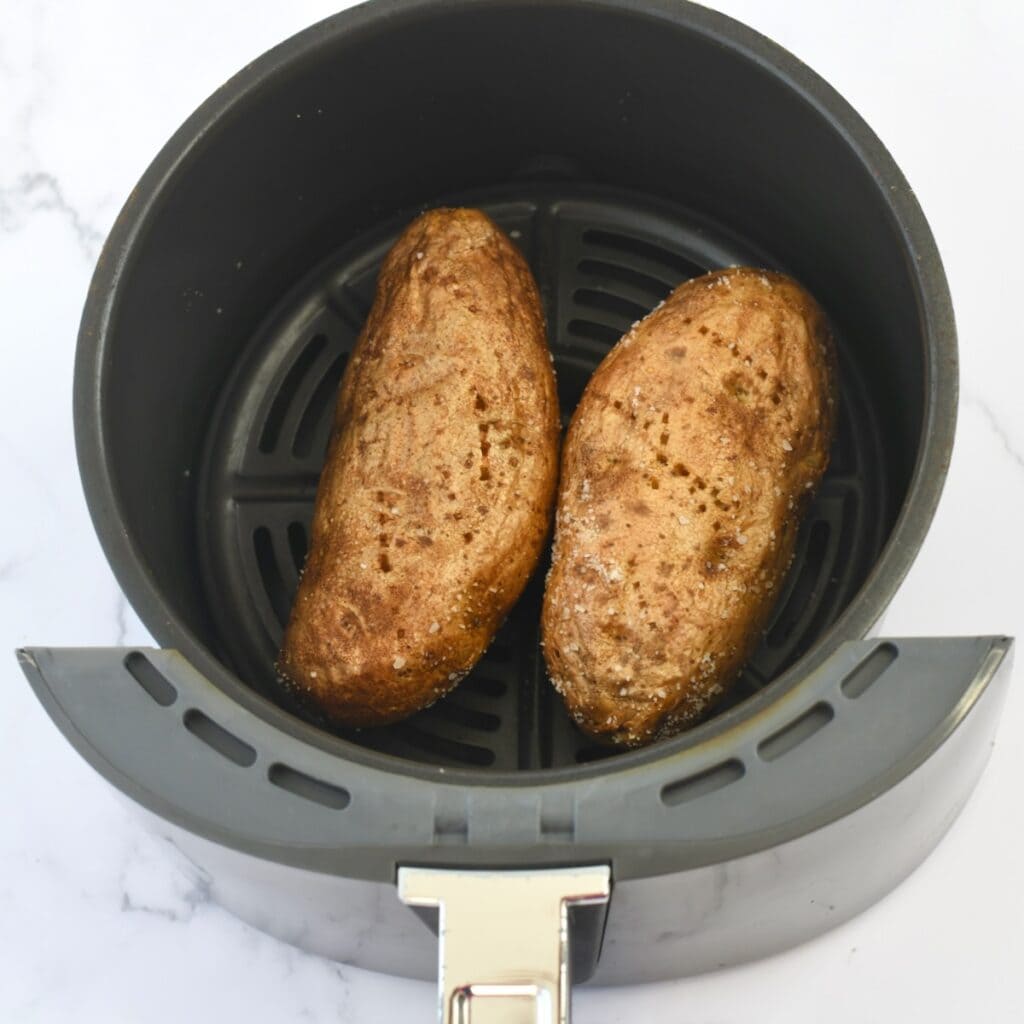 Cooked potatoes in the basket of an air fryer.