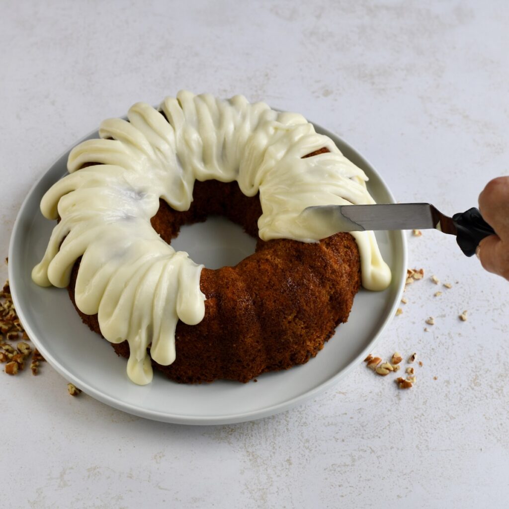 A white plate with carrot bundt cake and a hand with an offset spatula.