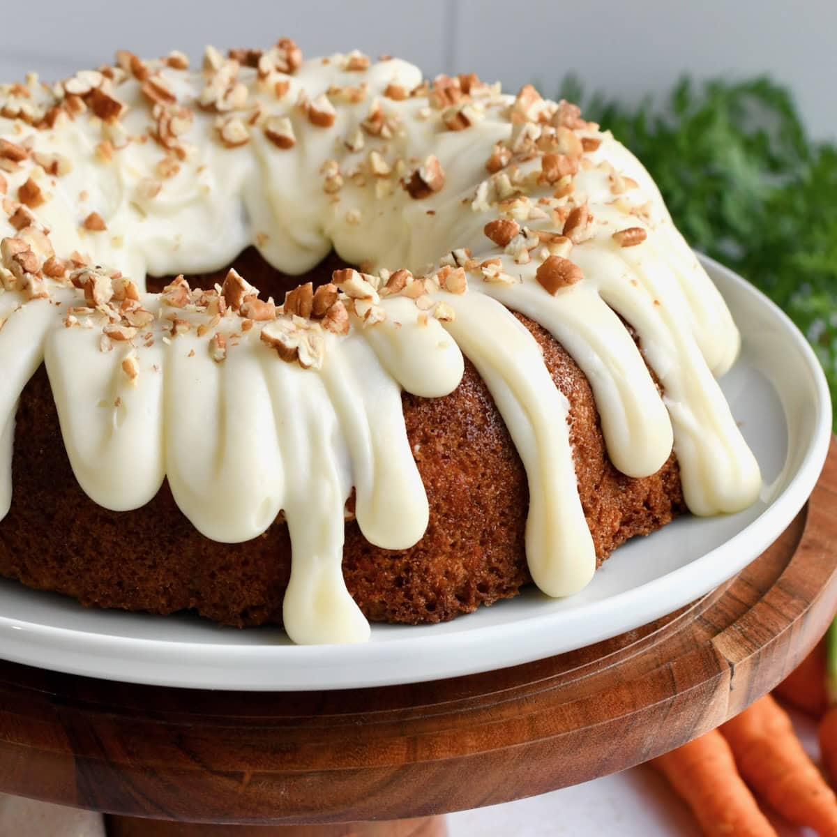 A side angle of carrot bundt cake on a white cake plate with a wooden cake stand.