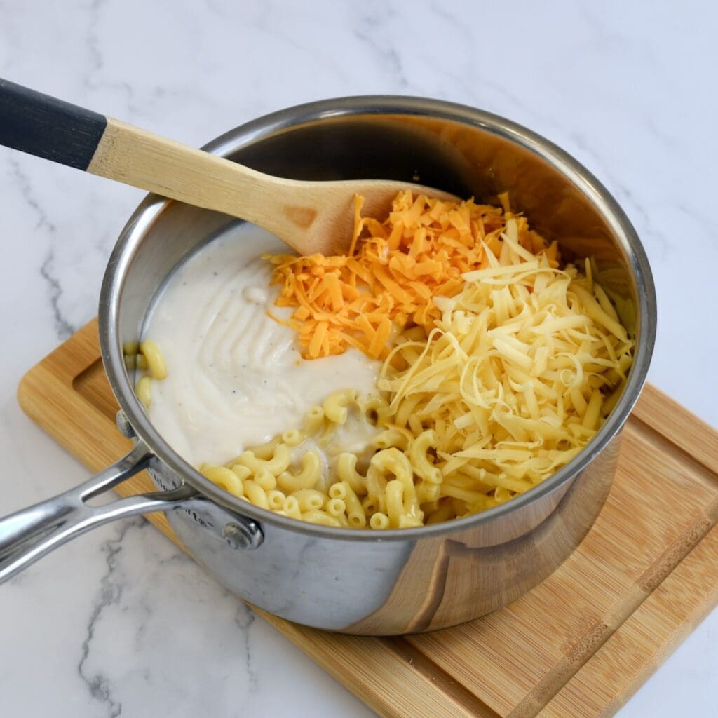 A metal saucepan with ingredients for gouda mac and cheese on a wooden board.