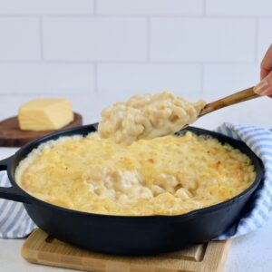 Gouda mac and cheese being scooped with a wooden spoon from a cast iron skillet.