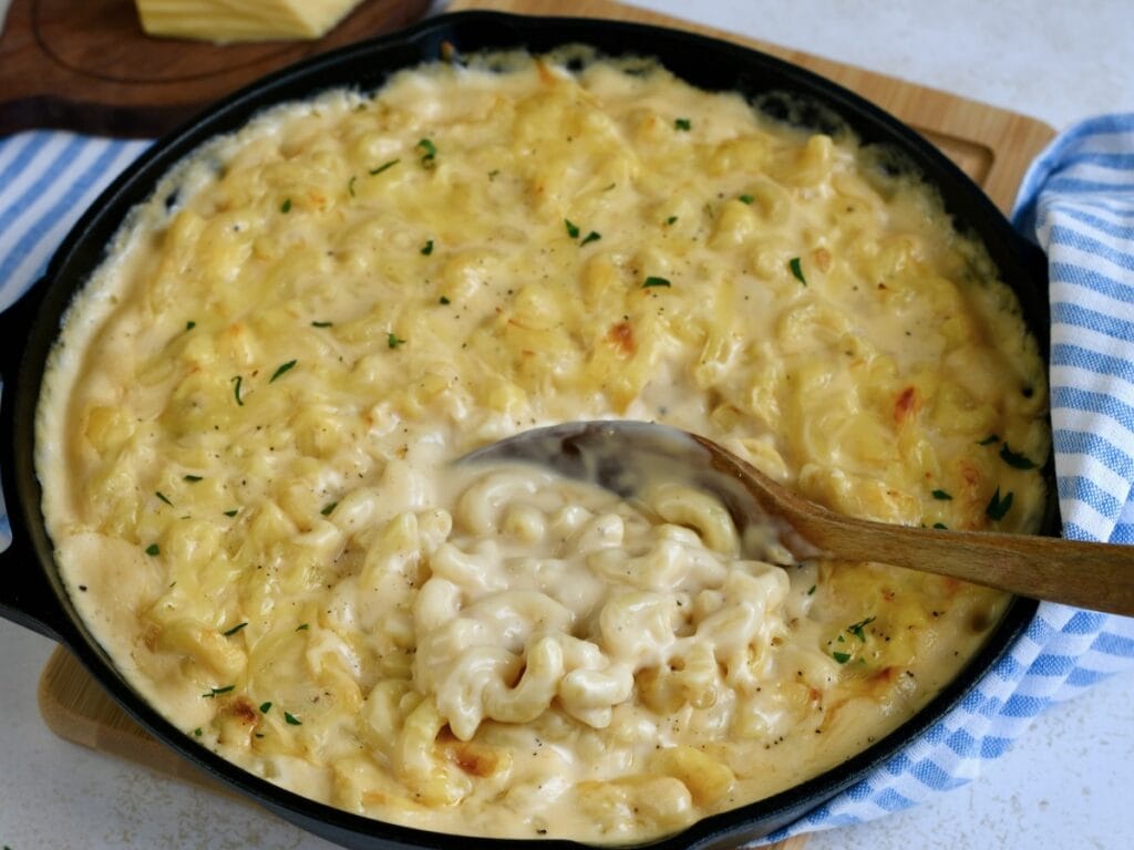 A cast iron skillet with gouda mac and cheese and a wooden spoon scooping some up.