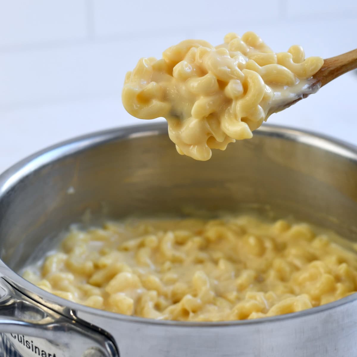 A metal saucepan with gouda mac and cheese with some being scooped up by a wooden spoon.