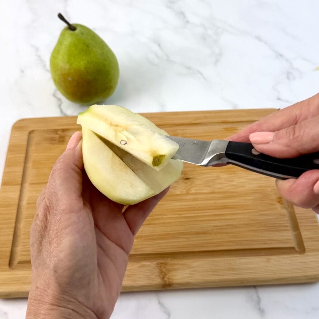 Hands holding a pear and a paring knife to take out the core of the pear.