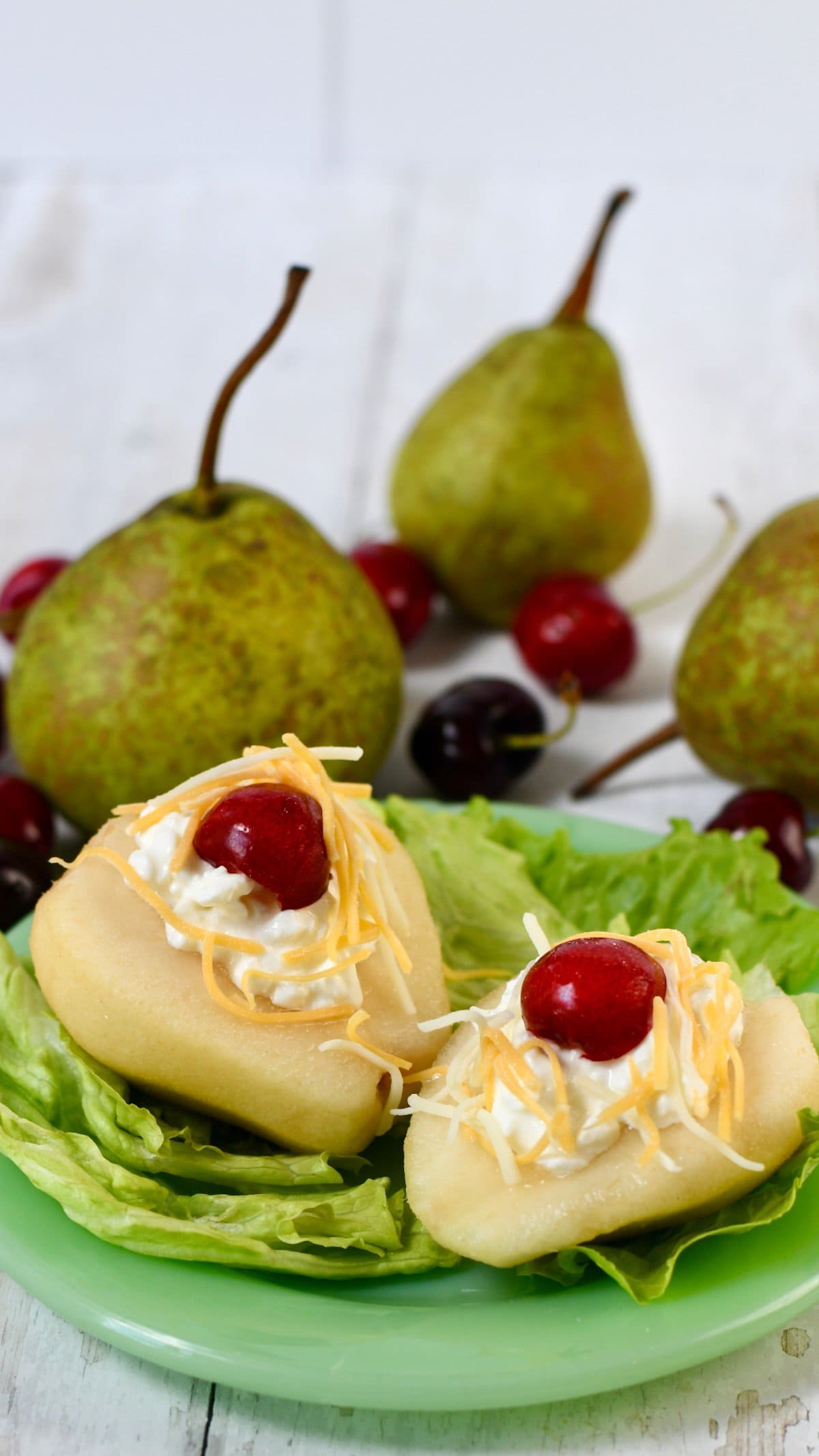 Southern pear salad with fresh pears on a plate lined with lettuce, then topped with cheese and cherries.