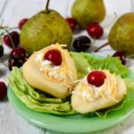 Two pears stuffed with cottage cheese, then garnished with shredded cheese and cherries on a plate.