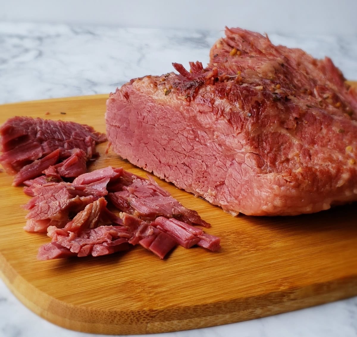 Corned beef shredded on a wooden cutting board.