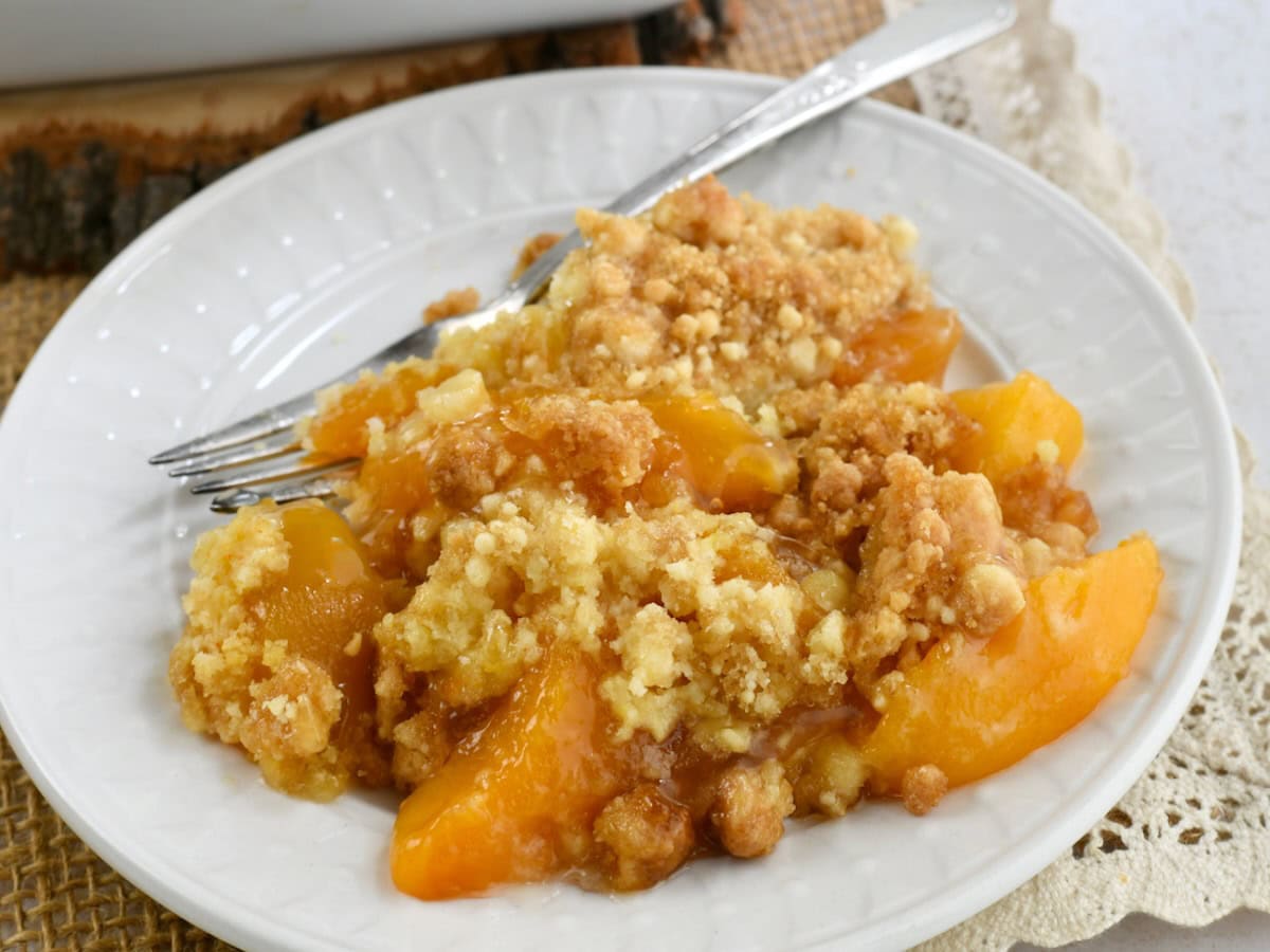 A white plate with cake mix peach cobbler with a fork resting on the plate.