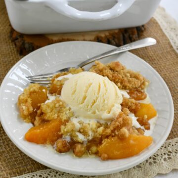 A white plate and fork with cake mix peach cobbler with a scoop of ice cream on top.