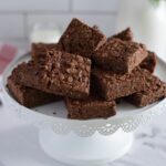 Chocolate rice krispie bars served on a white cake stand.