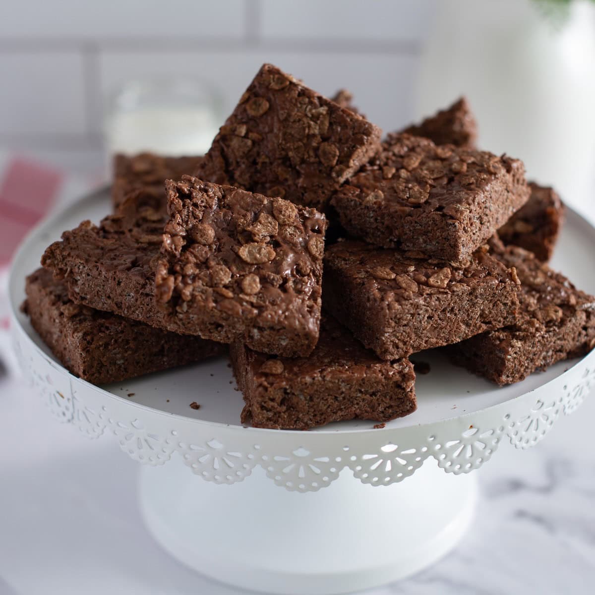 Chocolate rice krispie bars served on a white cake stand.