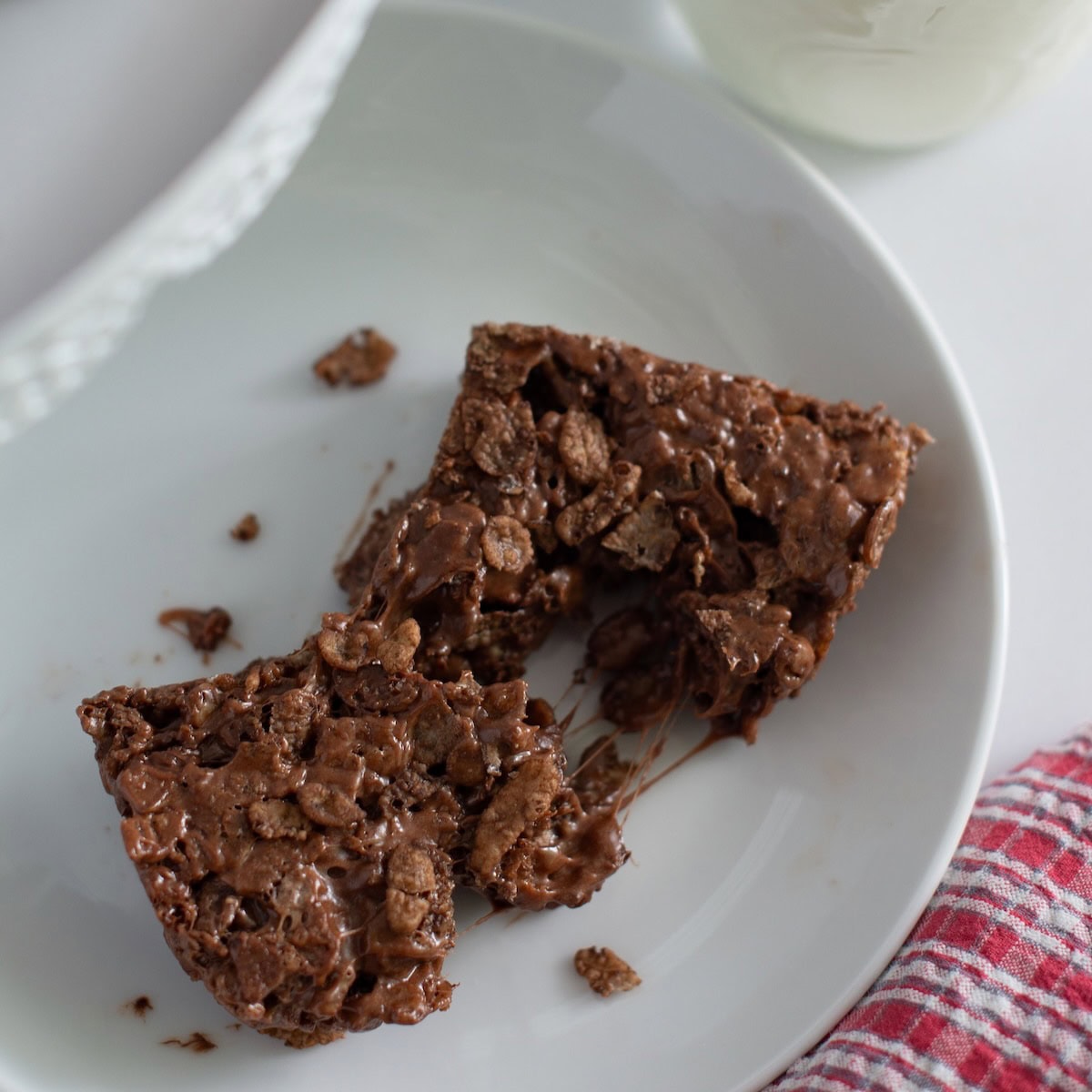 Chocolate rice krispie bar broken in half on a white plate.