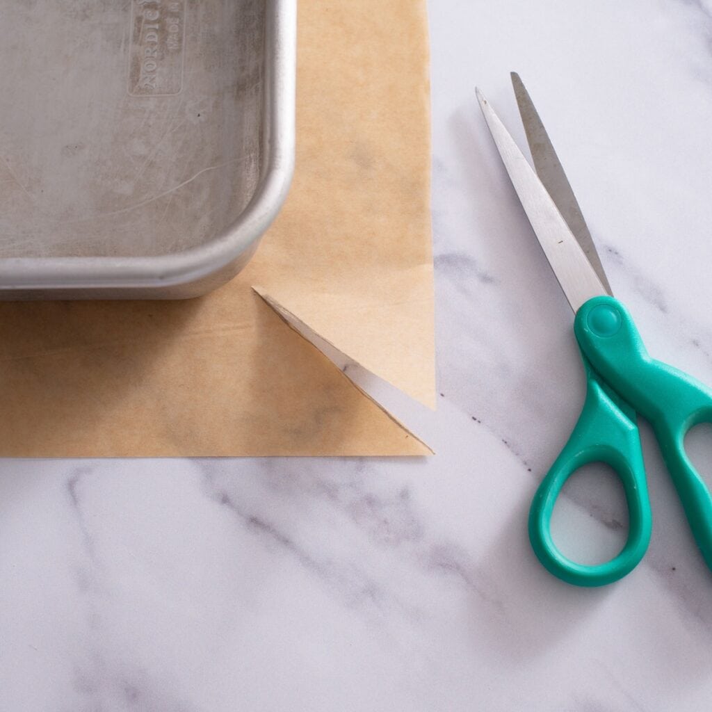Scissors next to a cut piece of parchment paper underneath the baking dish.