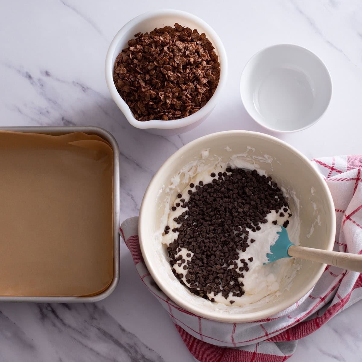 Folding chocolate chips into the melted marshmallows and butter in a bowl.