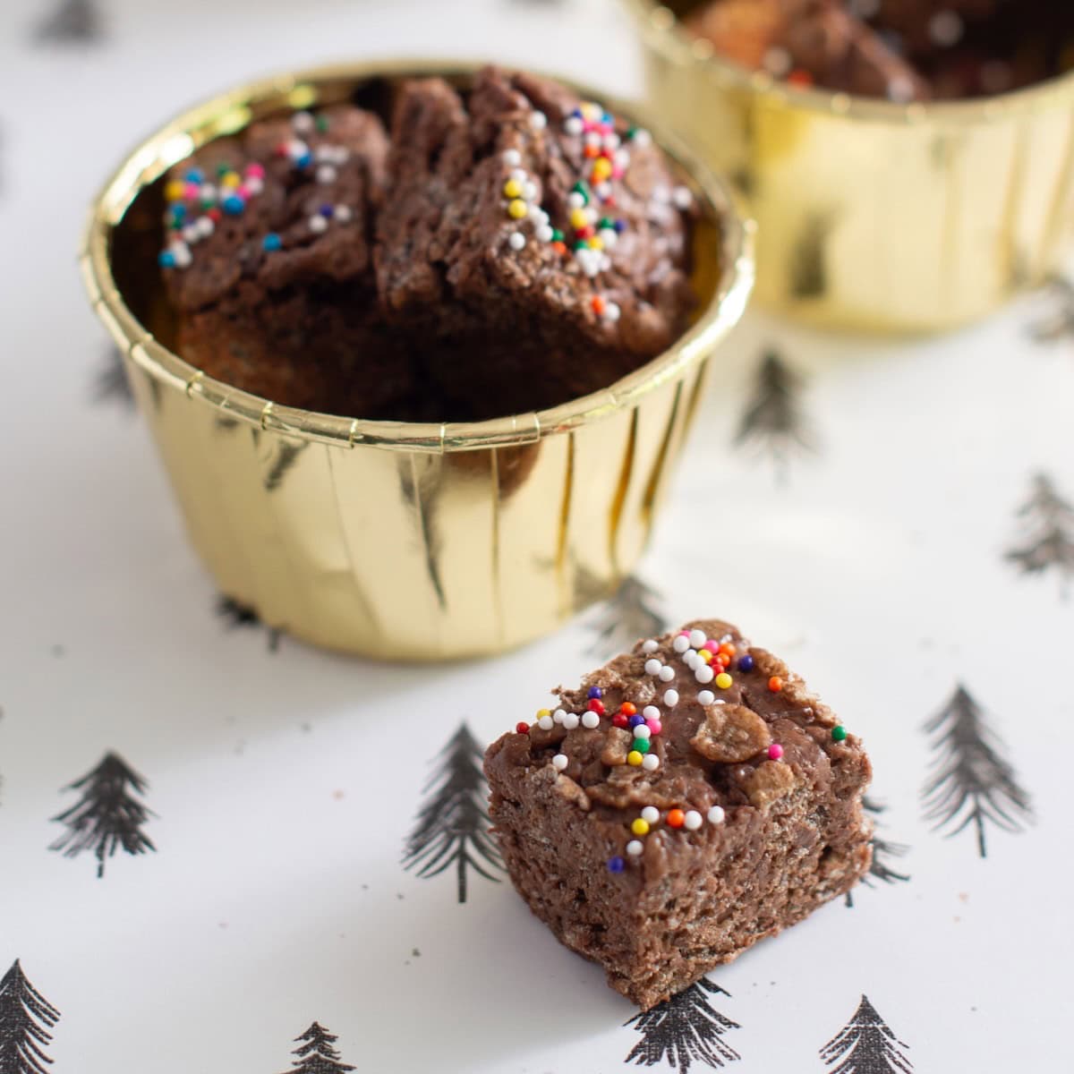 Chocolate Rice Krispies cut into bite size squares in gold foil candy cups.
