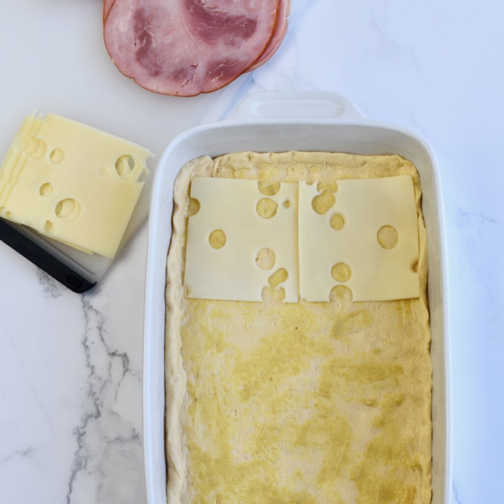 Layering Swiss cheese on top of the crescent roll dough in a baking dish.