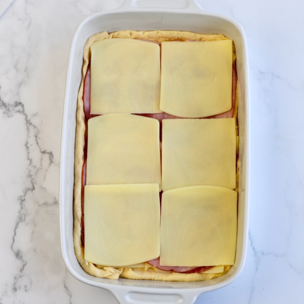 Layering cheese on top of the deli meats in a baking dish.