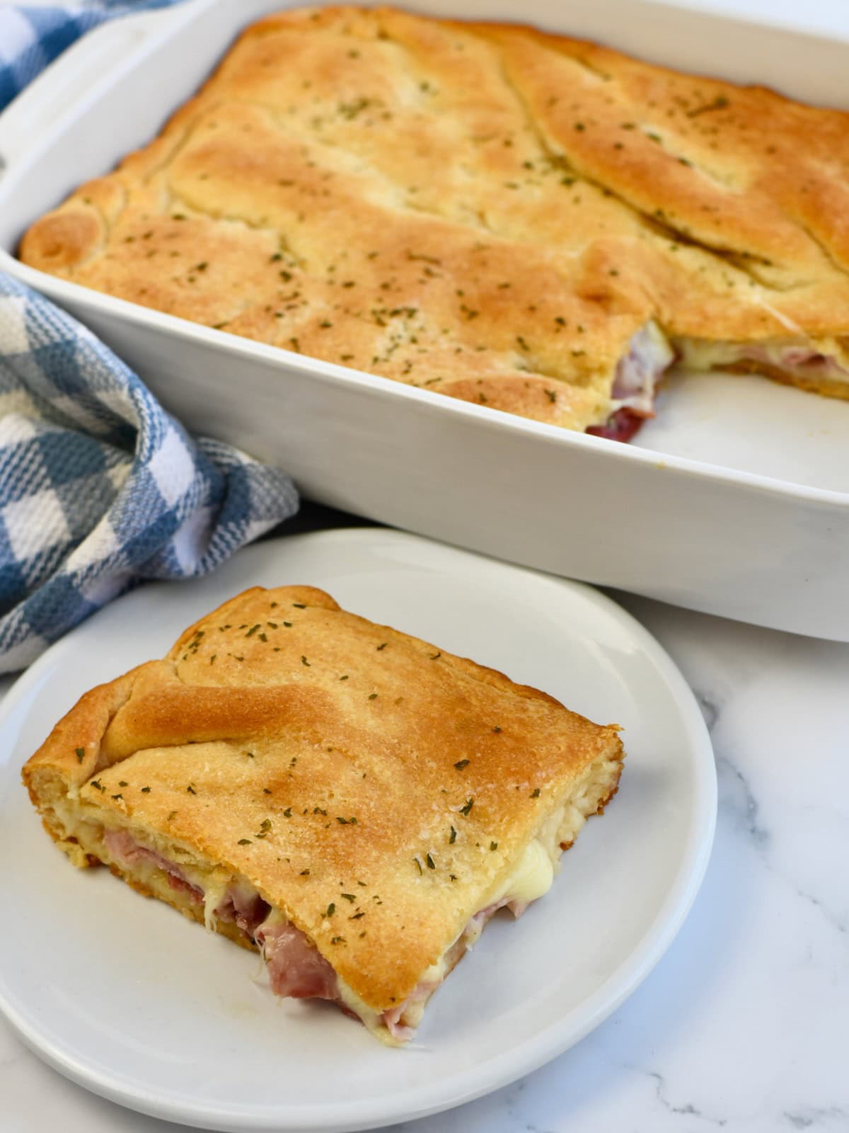 Portion of crescent roll ham and cheese bake served on a plate next to the baking dish.