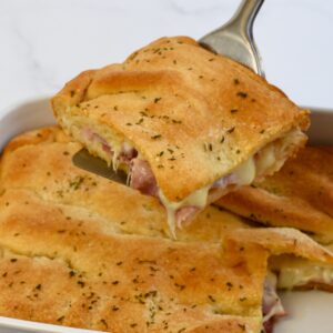 Metal spatula scooping up a portion of the crescent roll ham and cheese bake from the baking dish.
