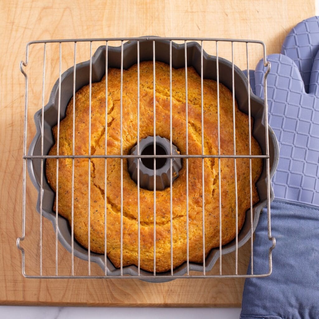 Baked orange poppy seed cake in a bundt pan with a cooling rack on top.