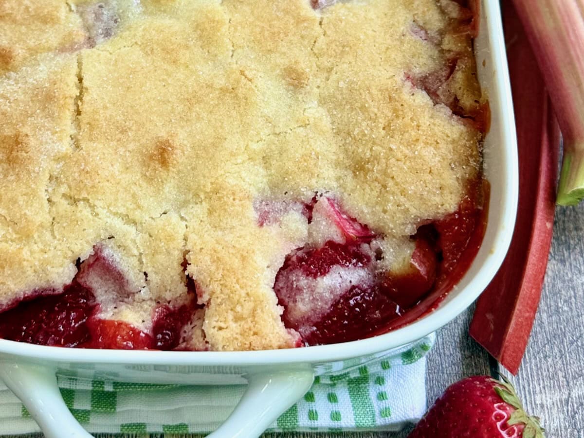 Corner of the strawberry rhubarb cobbler in a white baking dish.