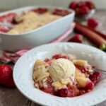 Strawberry rhubarb cobbler served in a bowl with a scoop of ice cream on top.
