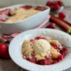 Strawberry rhubarb cobbler served in a bowl with a scoop of ice cream on top.