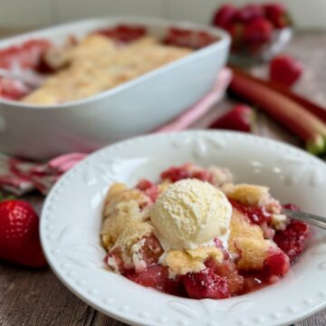 Strawberry rhubarb cobbler served in a bowl with a scoop of ice cream on top.