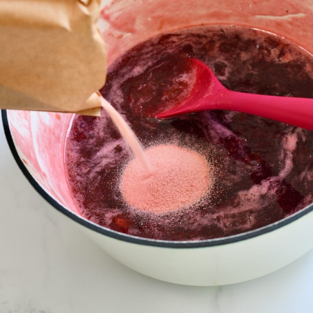 Pouring strawberry jello into the strawberry rhubarb mixture in a pot.