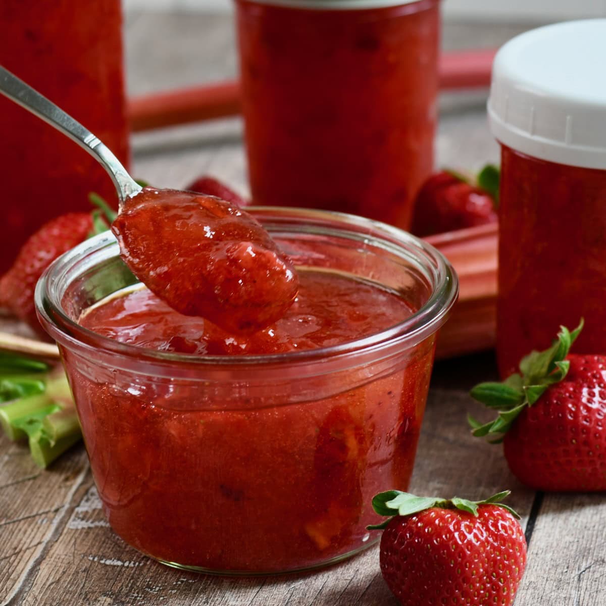 Strawberry rhubarb freezer jam in a glass container with a spoon scooping some up.