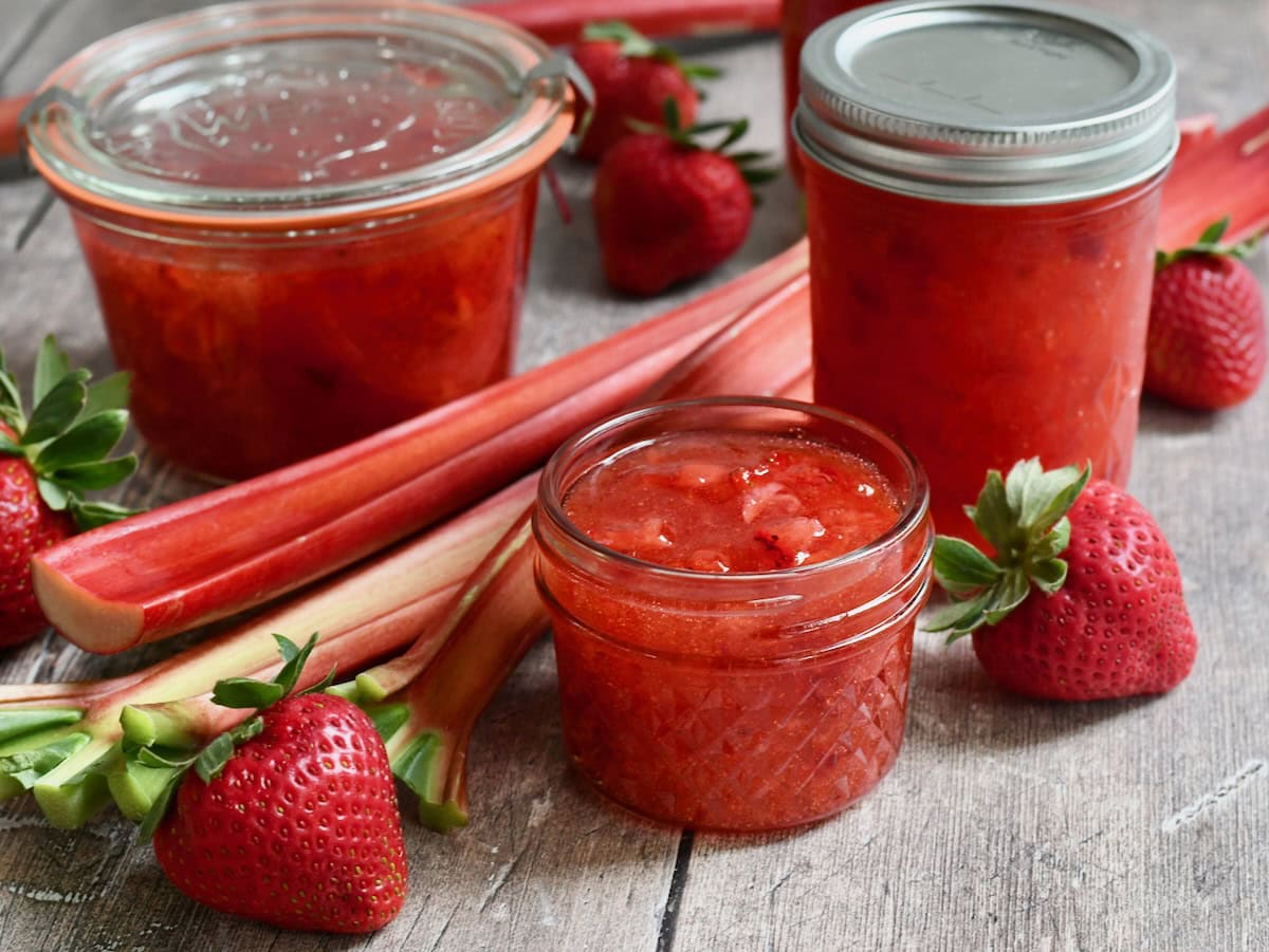 Side view of a few different containers of strawberry rhubarb freezer jam on a wooden background.