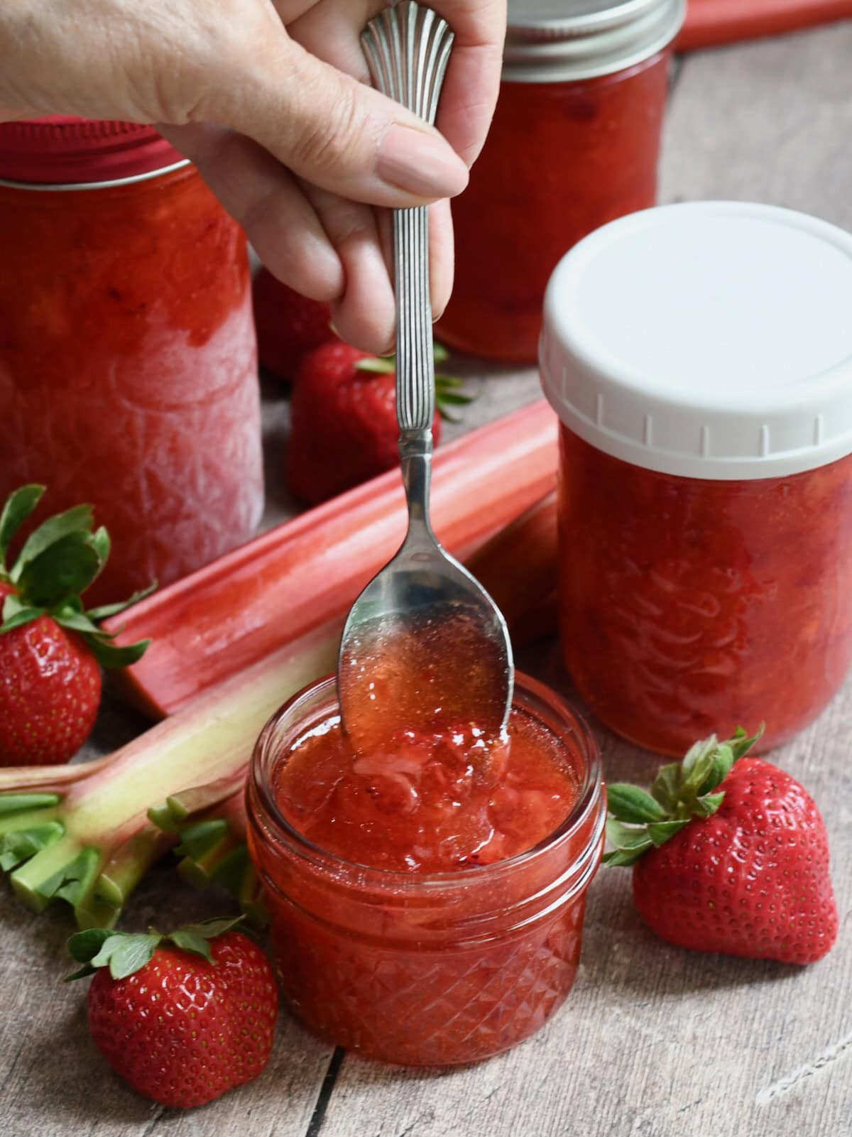 Hand holding a spoon, dipping it into a small jar of strawberry rhubarb freezer jam.