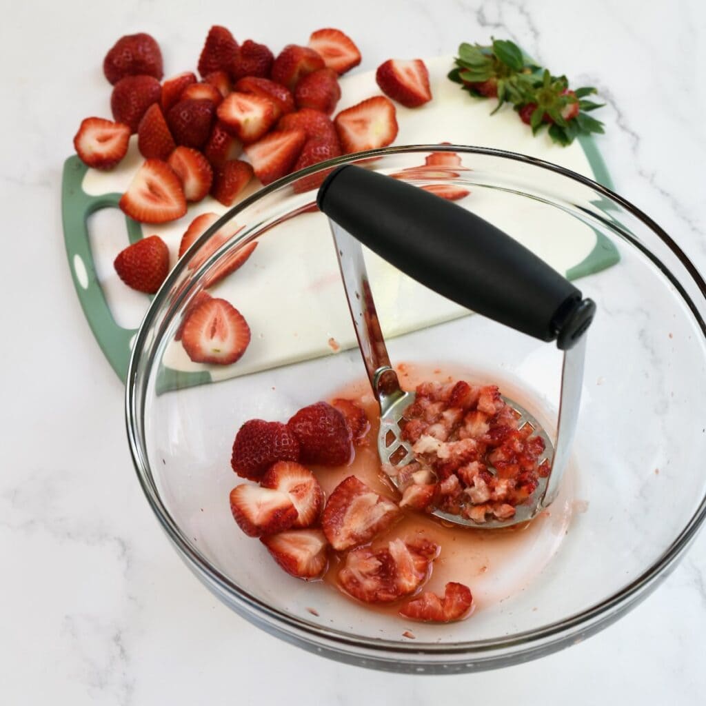 Mashing fresh strawberries with a potato masher in a bowl.